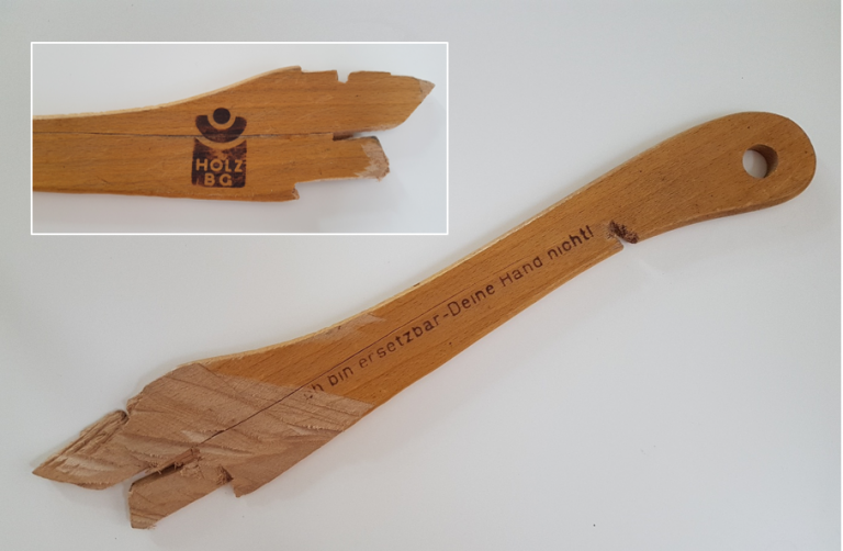 lädierter Schiebestock: Vorderseite "Ich bin ersetztbar - Deine Hand nicht!" und Rückseite mit Logo der ehemaligen BG Holz