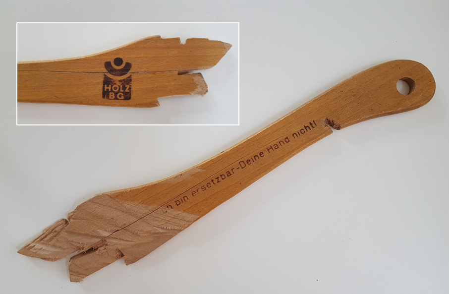 lädierter Schiebestock: Vorderseite "Ich bin ersetztbar - Deine Hand nicht!" und Rückseite mit Logo der ehemaligen BG Holz